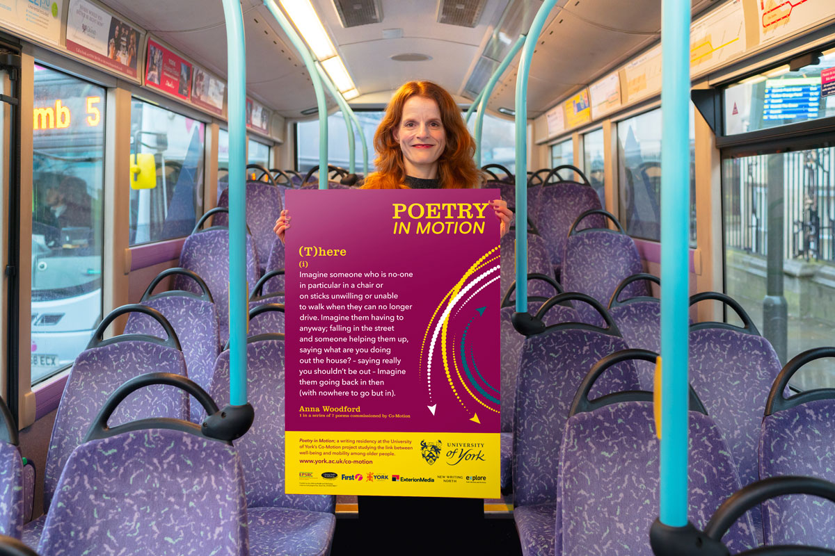 Anna Woodford stands in a bus aisle holding her poetry poster